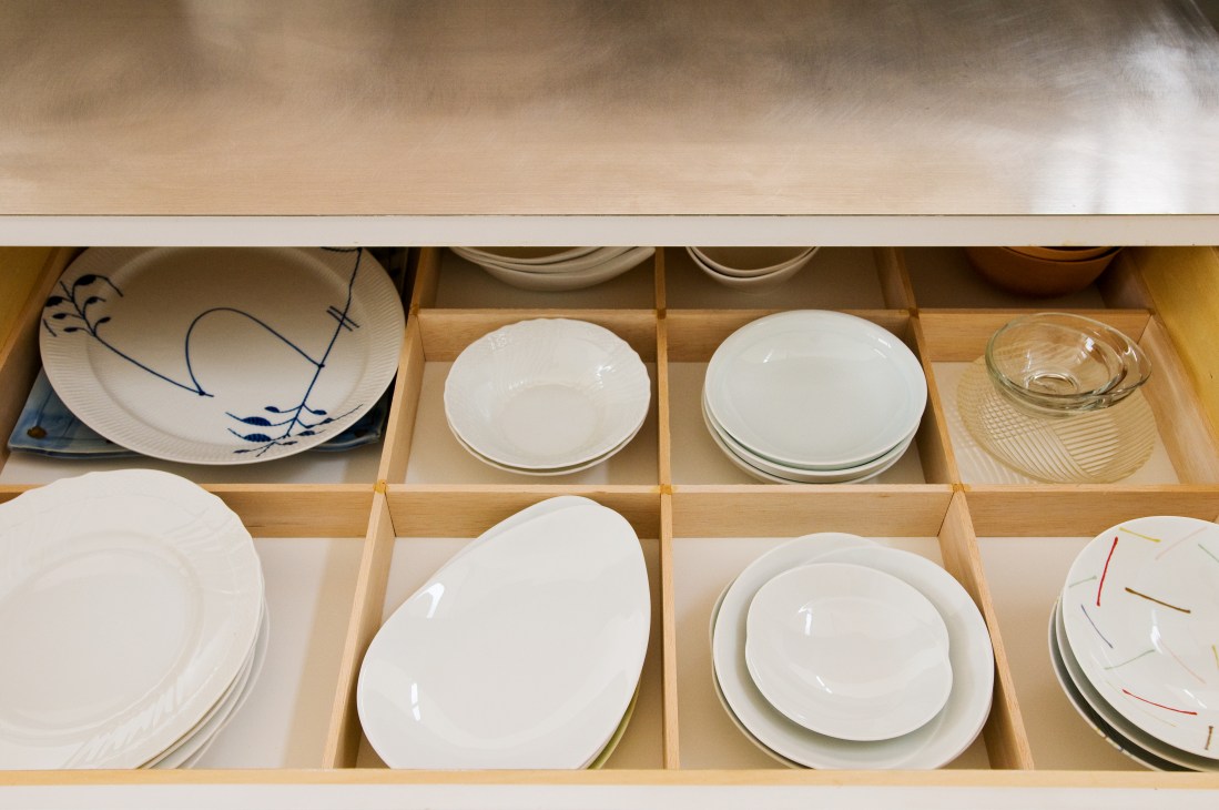 Wooden drawer divider organizing white plates and bowls in neat compartments.