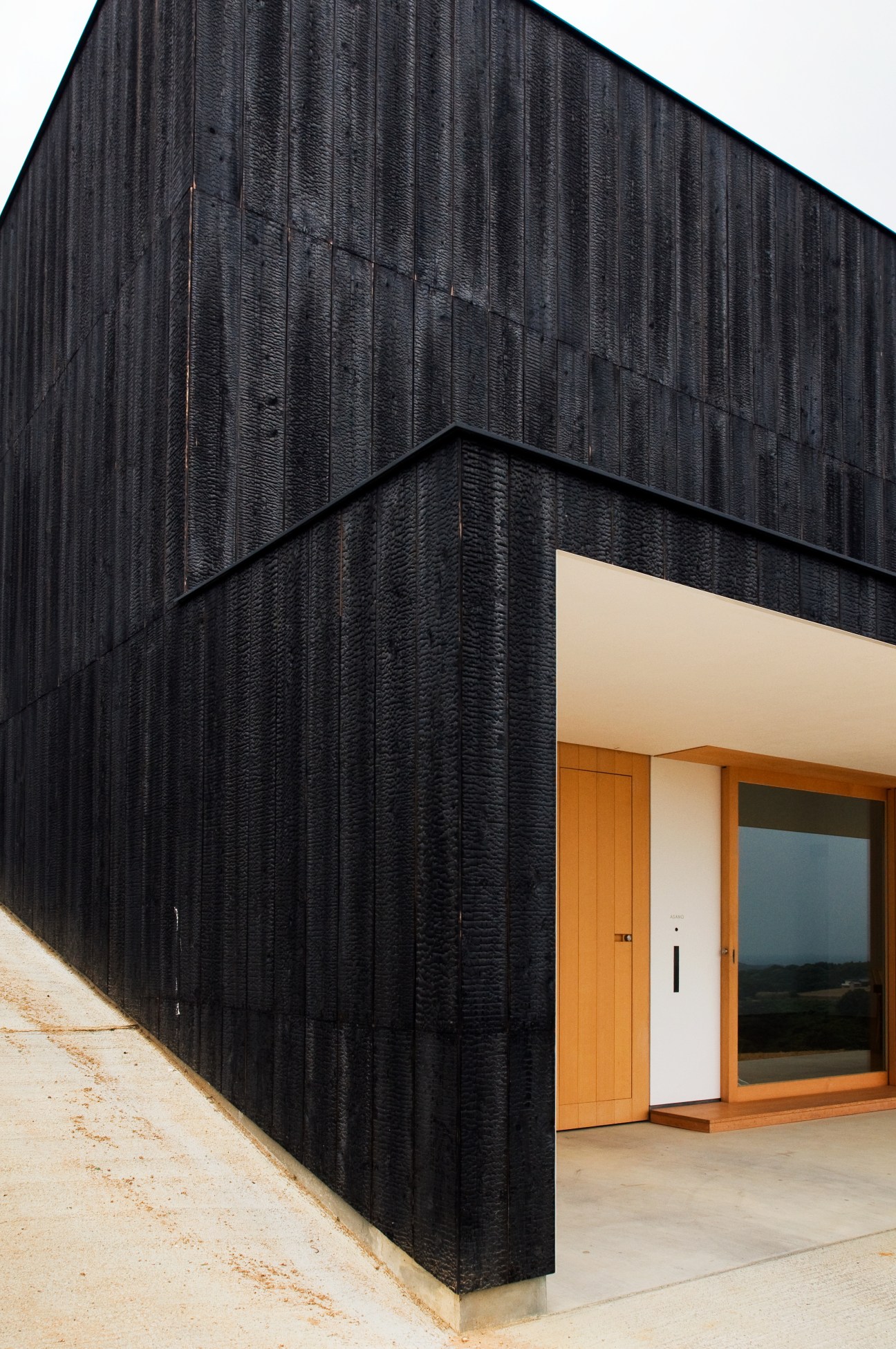 Close-up of black burnt cedar cladding with orange wooden door and white panel entrance.