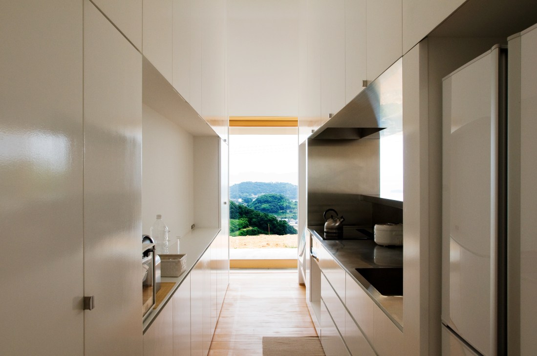 Minimalist kitchen with white cabinetry and countryside view through large window.