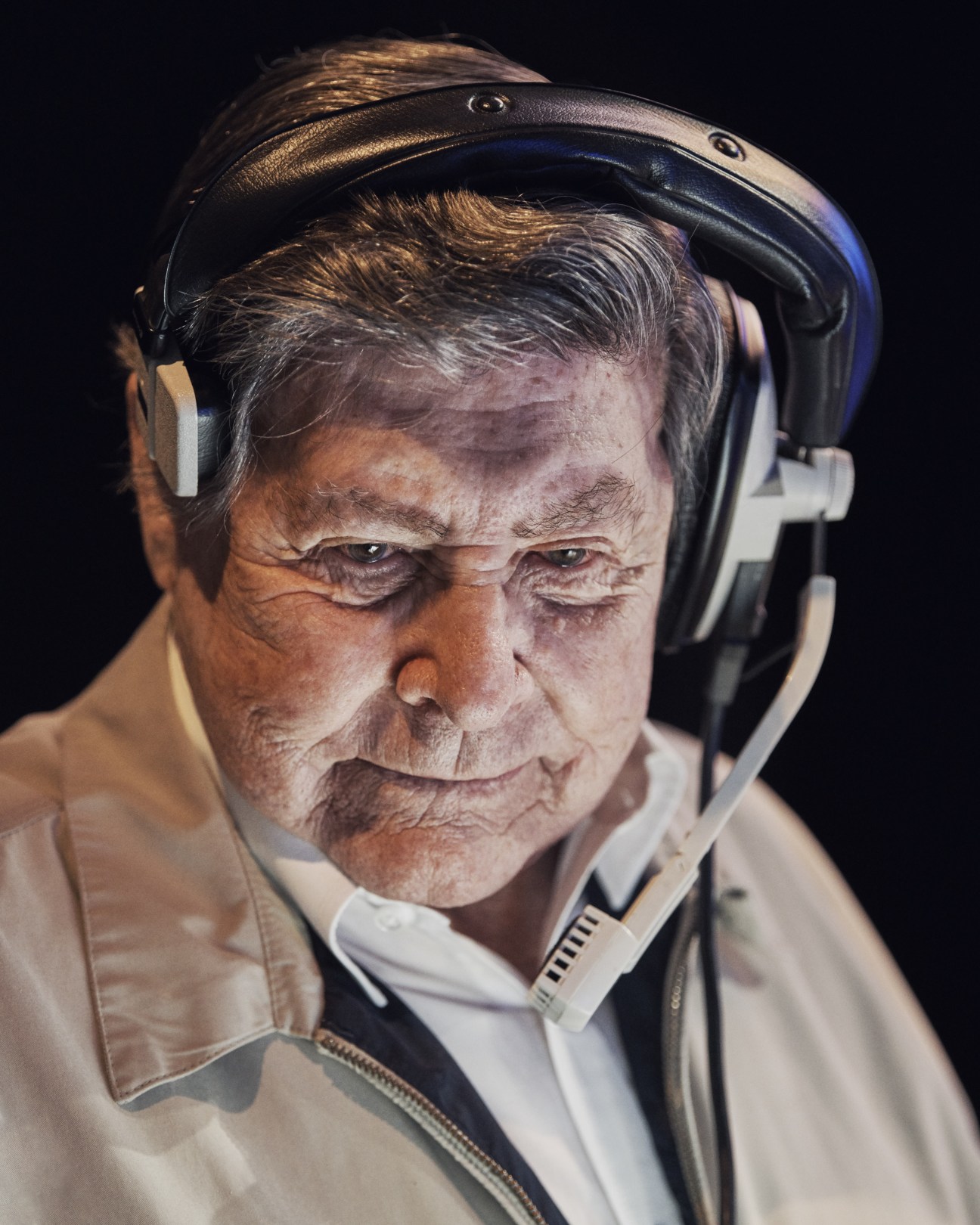 Johnny Gilbert, Jeopardy! announcer, wearing headphones and looking downward