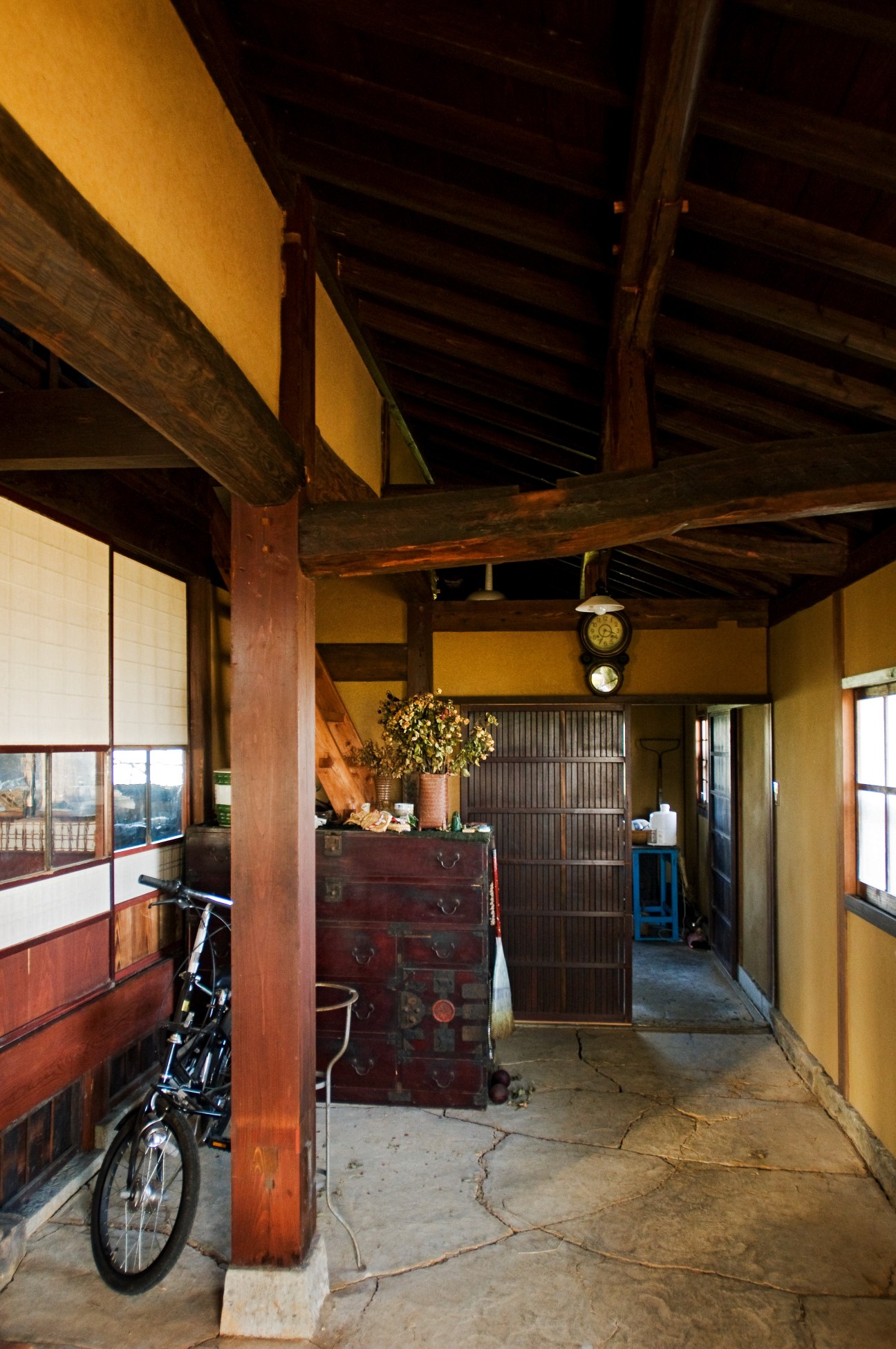 Interior of a traditional Japanese farmhouse entrance hall with wooden beams, yellow walls, and vintage furniture.