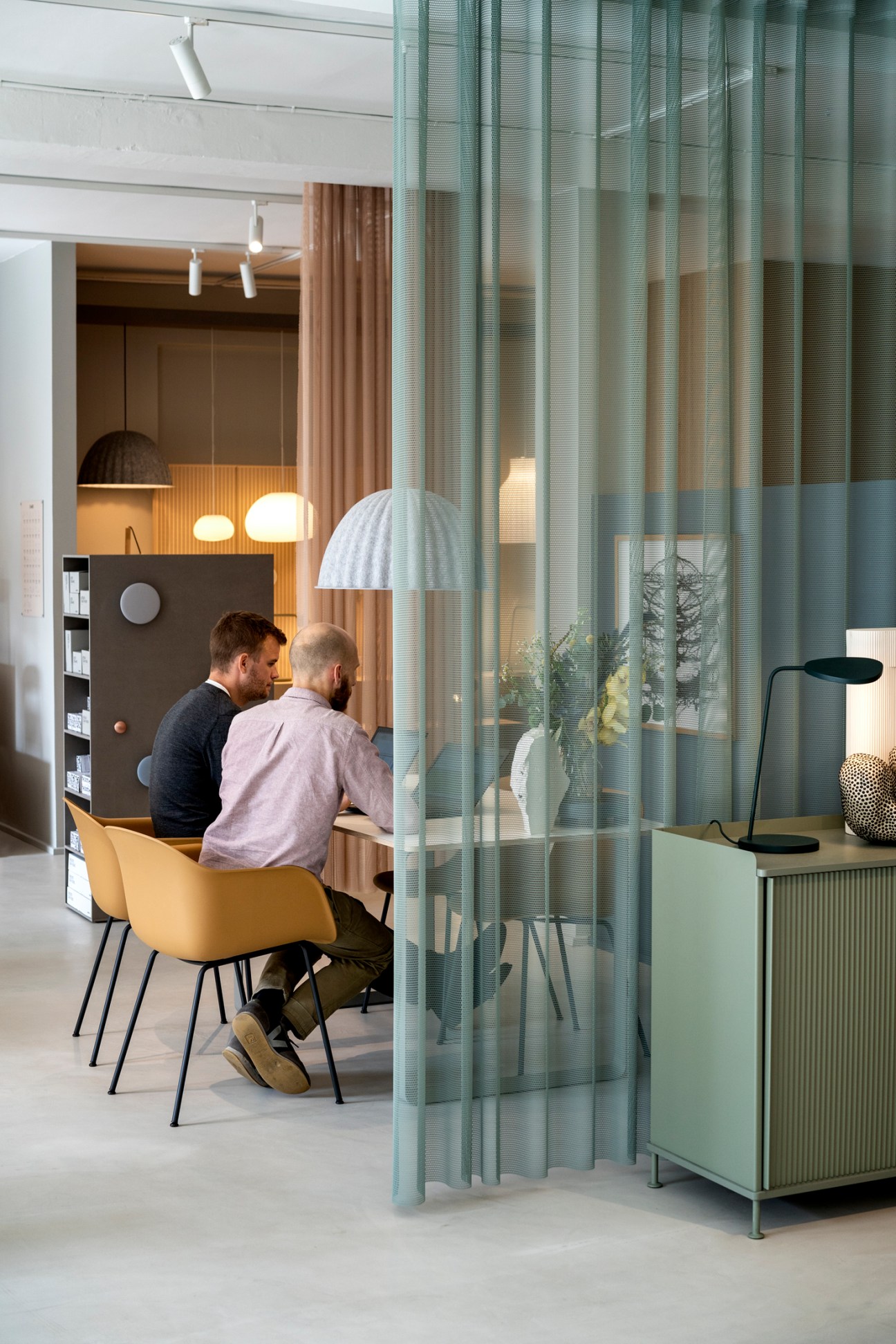 Two men in business attire sit at wooden table in modern office with glass partition and design furniture