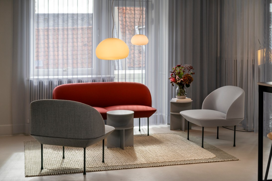 Modern seating arrangement with rust-colored sofa, gray and beige chairs around small table under pendant lights