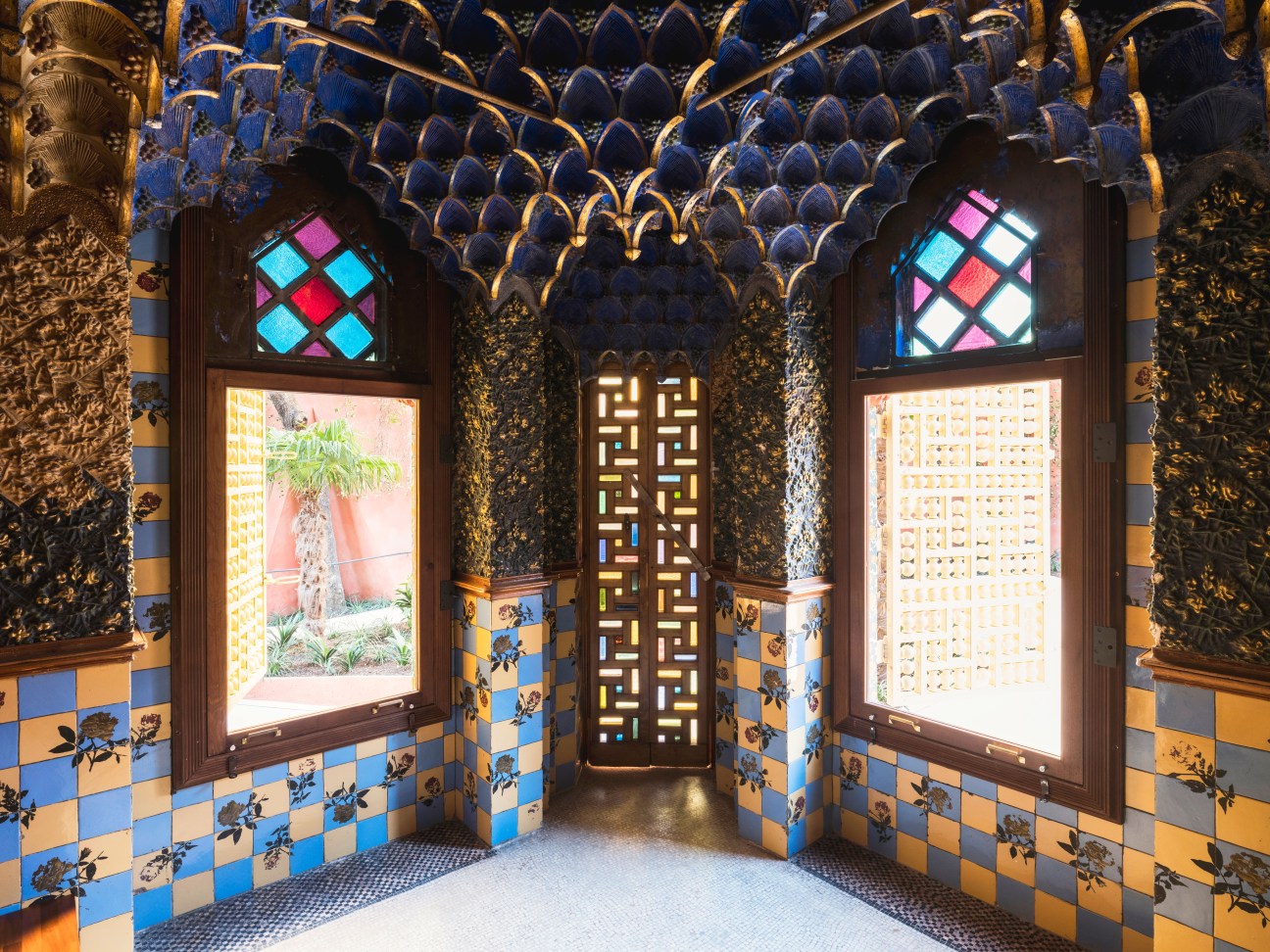 Casa Vicens smokers' room with ornate blue and gold ceiling, hand-painted tile walls in blue and yellow checkerboard pattern, and stained glass windows.