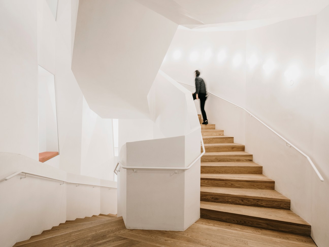 Person ascending a modern wooden staircase with white walls and minimalist design in Casa Vicens.