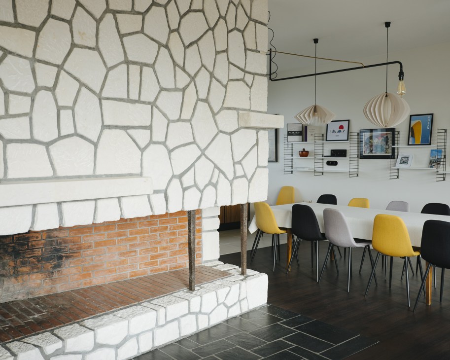 Modern interior with geometric wall pattern, pendant lights, and colorful mid-century chairs at a dining table.