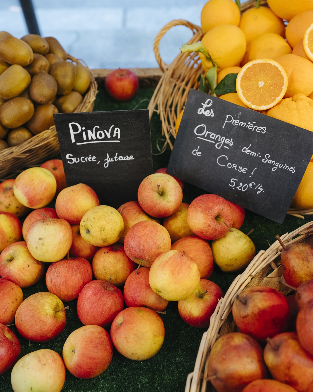 Colorful apples and oranges displayed at a French farmers market with handwritten price signs.