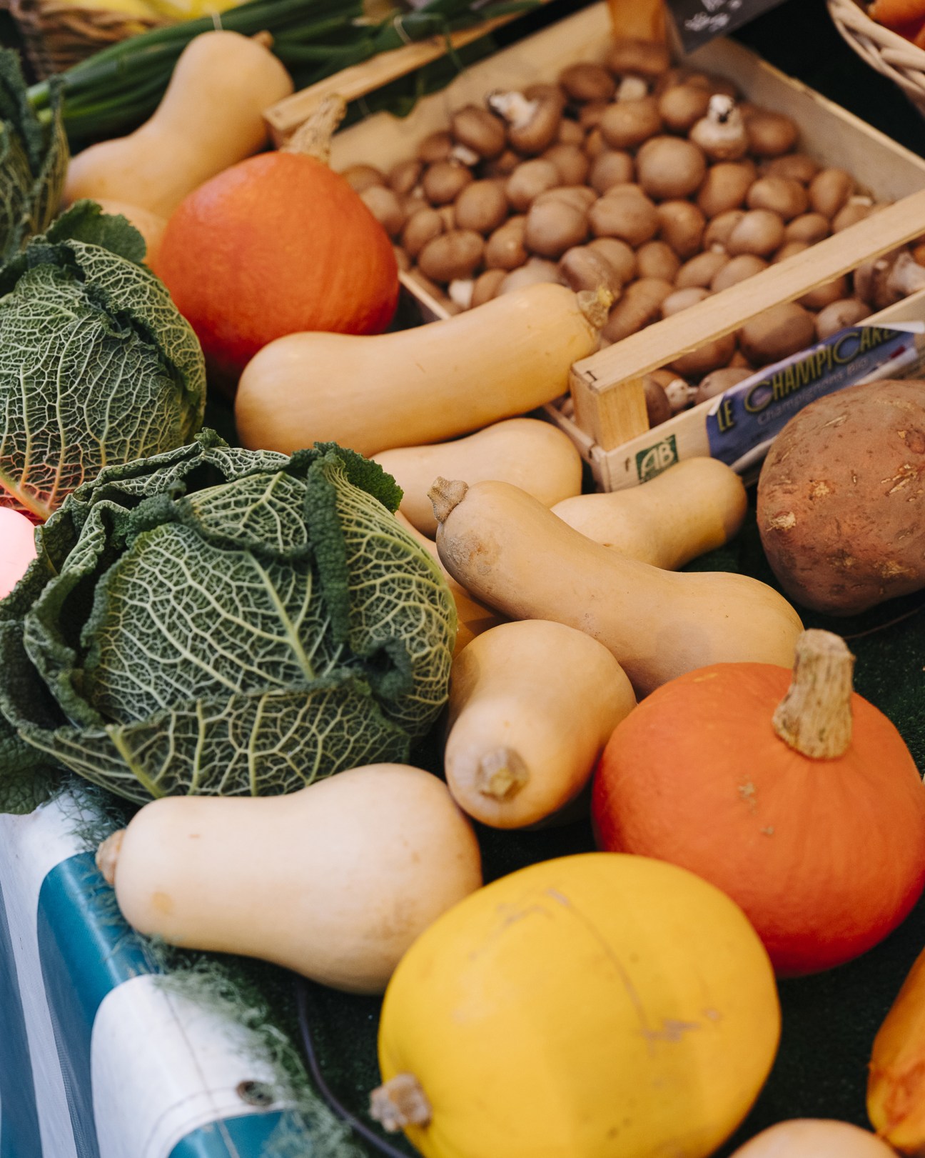 Organic vegetables including cabbage, squash, pumpkins, and chickpeas in wooden boxes at a farmers market.