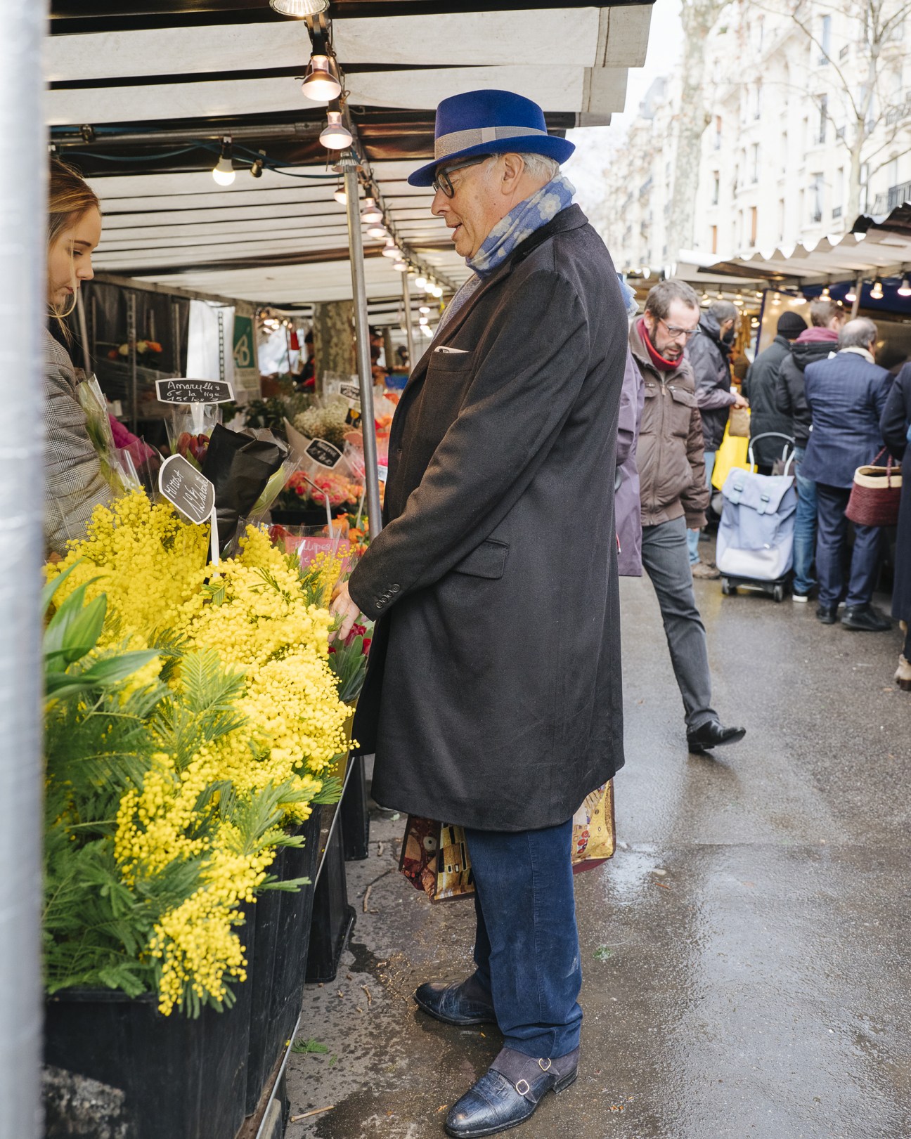Elderly man in blue hat shopping at flower stall with yellow blooms at Boulevard Raspail market