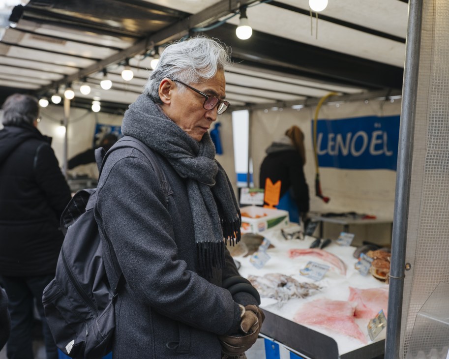 Older man examining fresh fish at a market stall with blue signage.