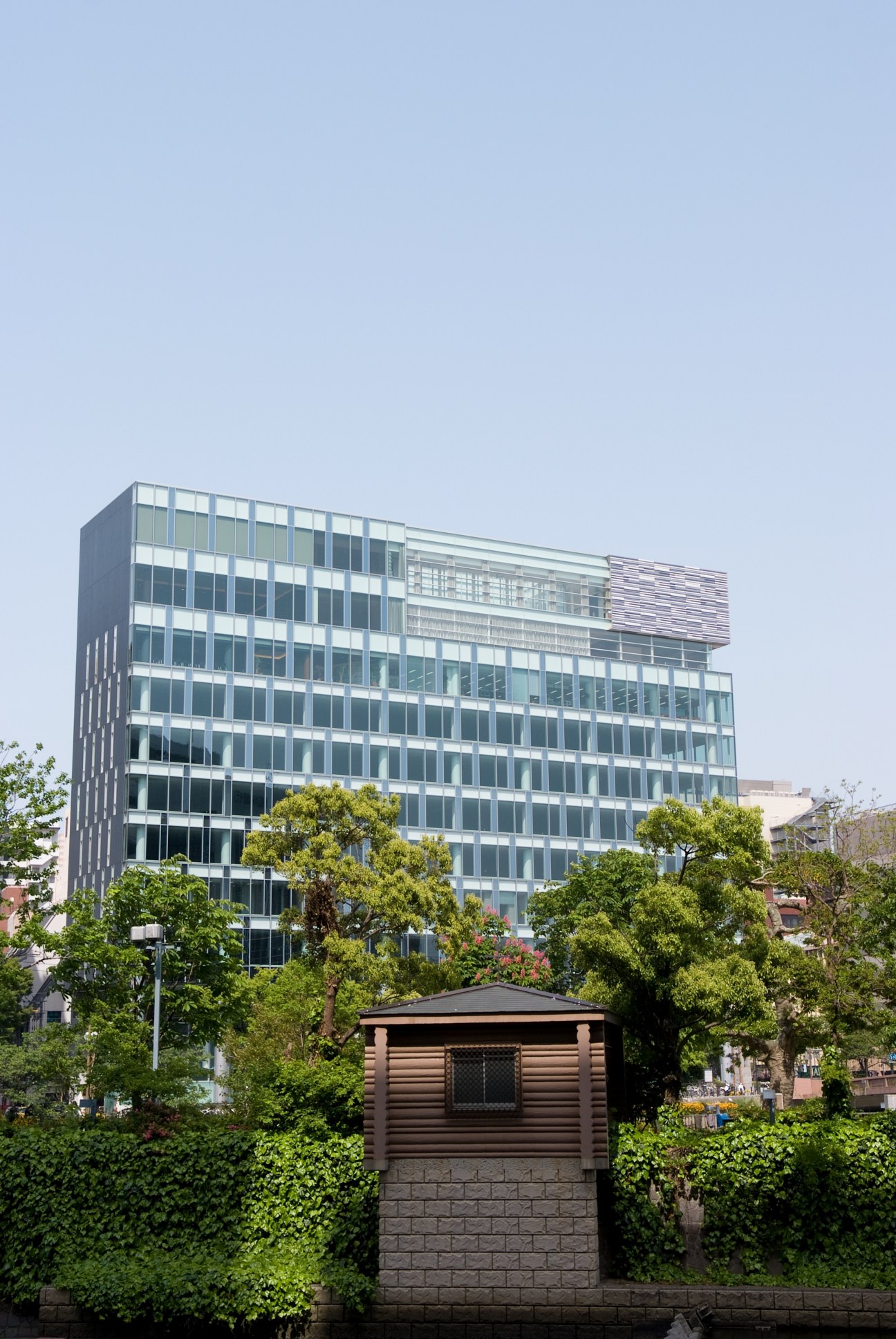 Modern multi-story office building with glass and white facade near riverside greenery in Nakasu.