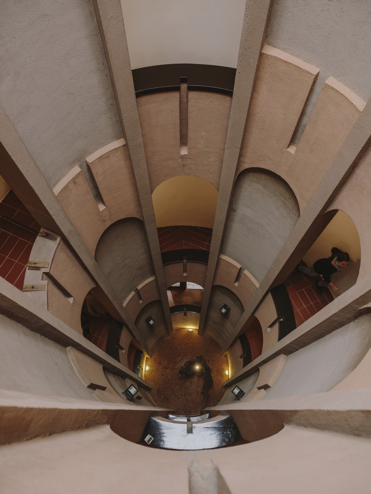 Spiral staircase inside converted concrete silo with whitewashed walls and multiple floor openings.