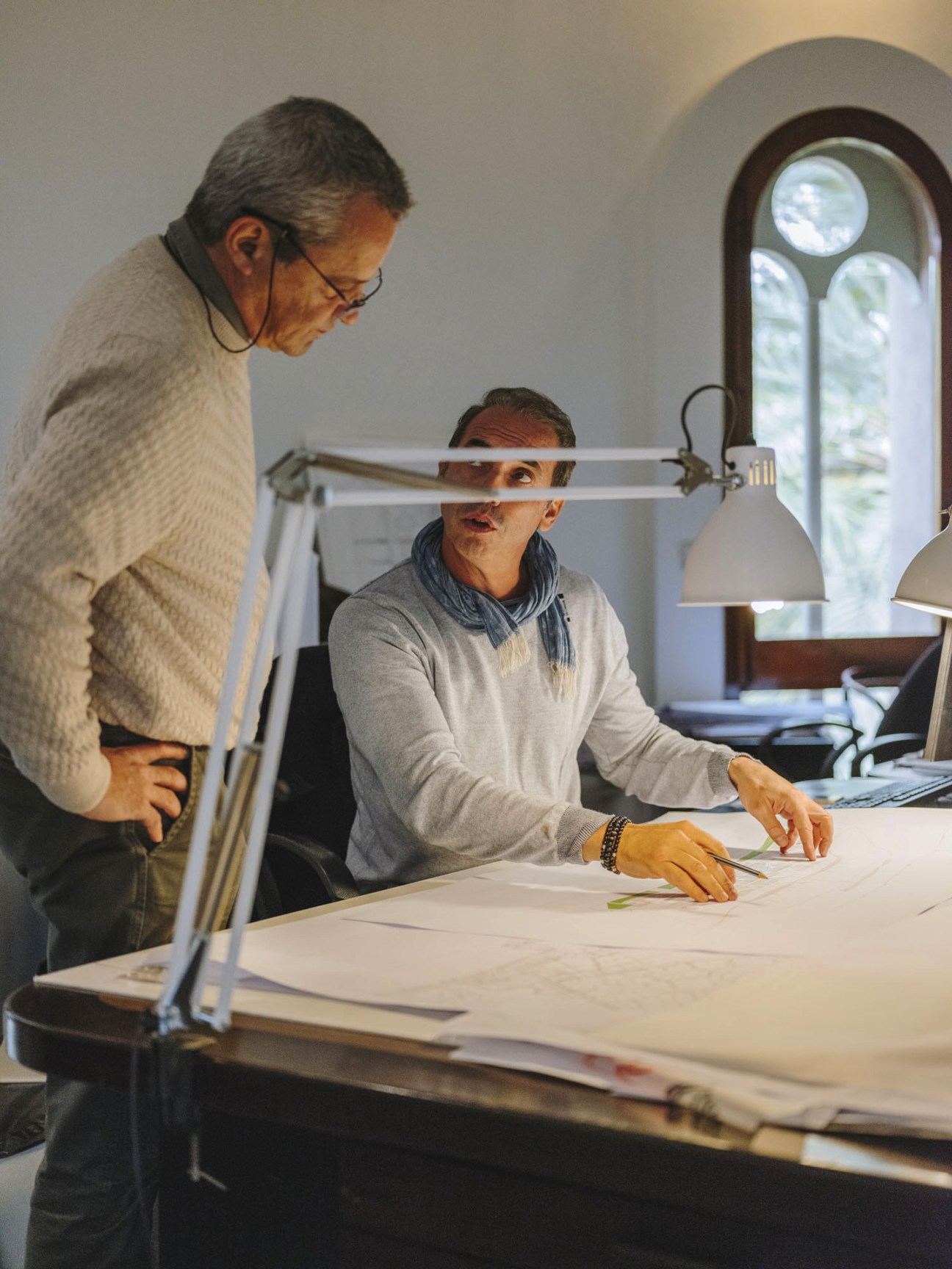 Gabor Somssich in discussion with a colleague at a desk with architectural plans and lamp