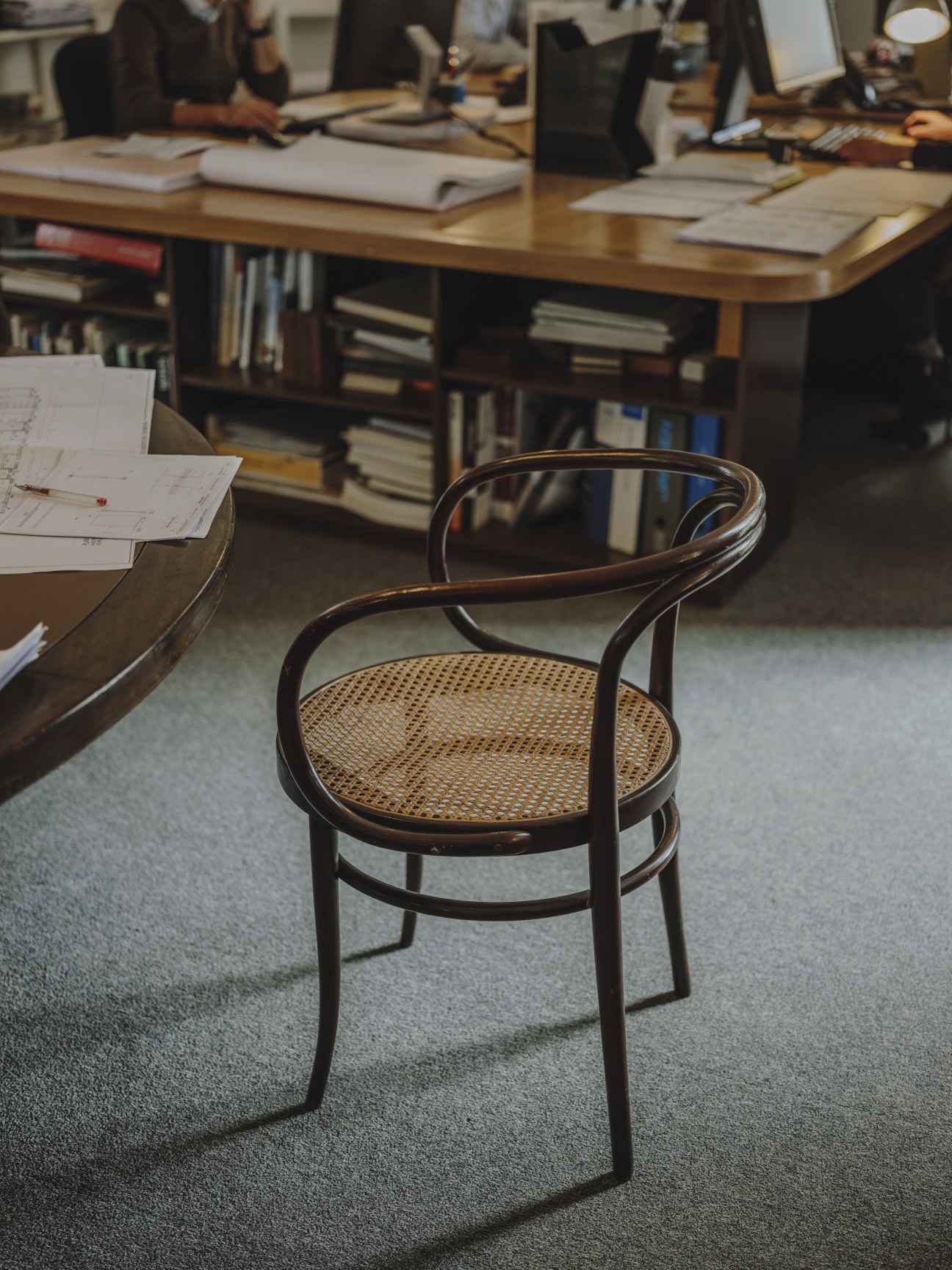 Bentwood Thonet chair with rattan seat in an office workspace with architectural plans and desk visible in background.