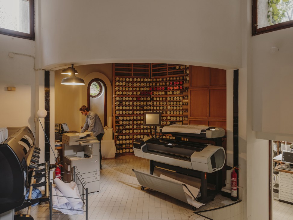 Basement archive room with architectural documents stored on wooden shelving and printing equipment.