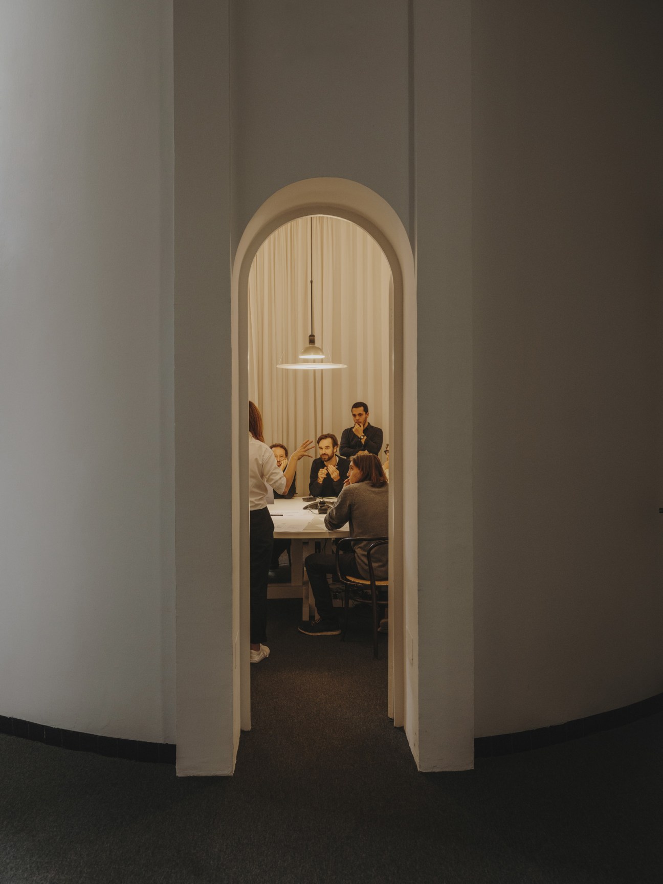 Team members meeting in a whitewashed silo office space with arched doorway and pendant light.