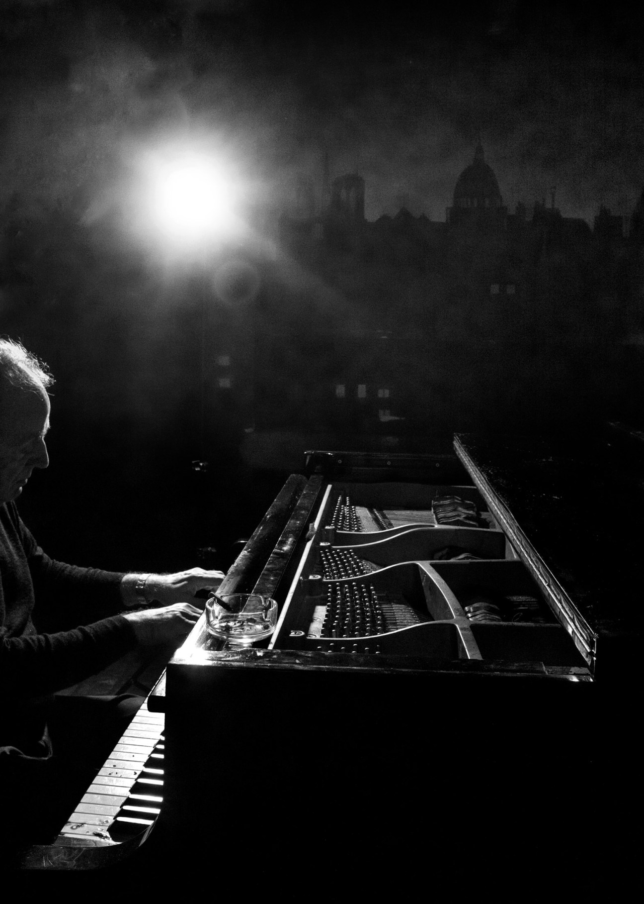 Pianist performing at Kawai grand piano in smoky Chez Castel basement with Paris cityscape visible through window