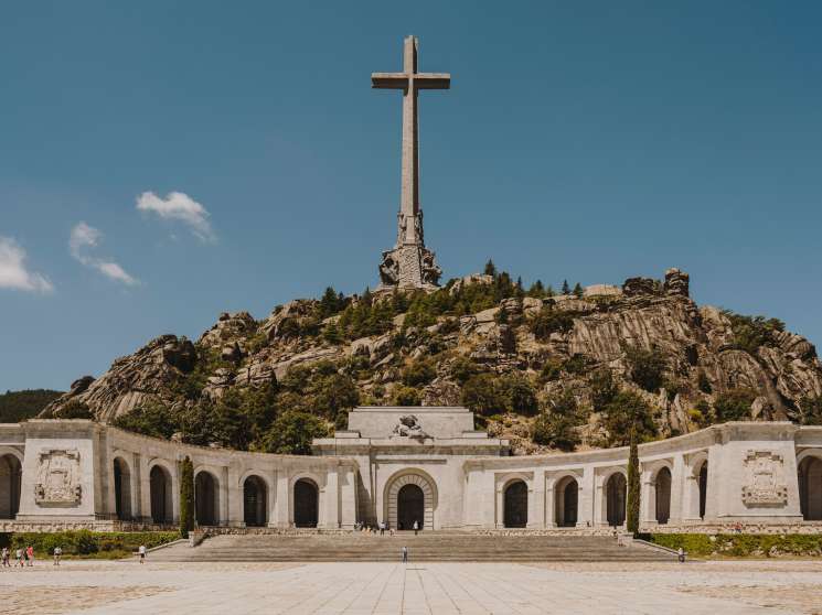 A 130-metre-tall stone cross atop a rocky mountain with a white basilica building below at Valle de los Caidos.