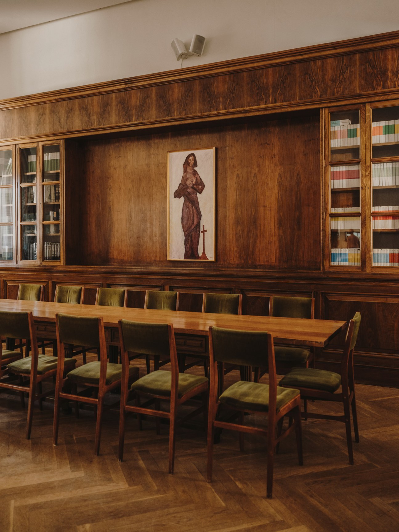 Wooden library interior with bookshelves, desk, and portrait painting, representing the monastery's scholarly space.