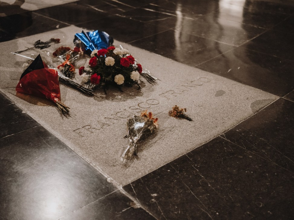 Franco's tomb covered with red and white flower bouquets and a blue ribbon on a stone floor.