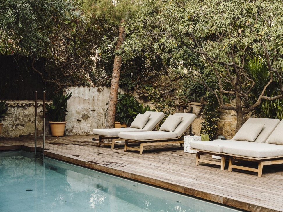 Swimming pool in hotel garden surrounded by mature trees and wooden deck with loungers.
