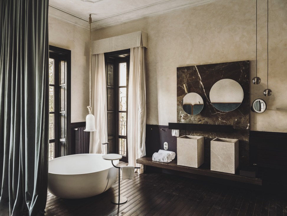 Luxurious bathroom with freestanding white tub, dark marble wall with circular mirrors, and cream storage boxes.