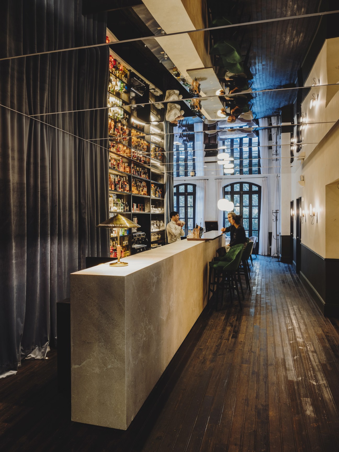 Interior corridor with long counter bar, dark curtains, backlit shelving, and mirrored ceiling reflecting garden views.