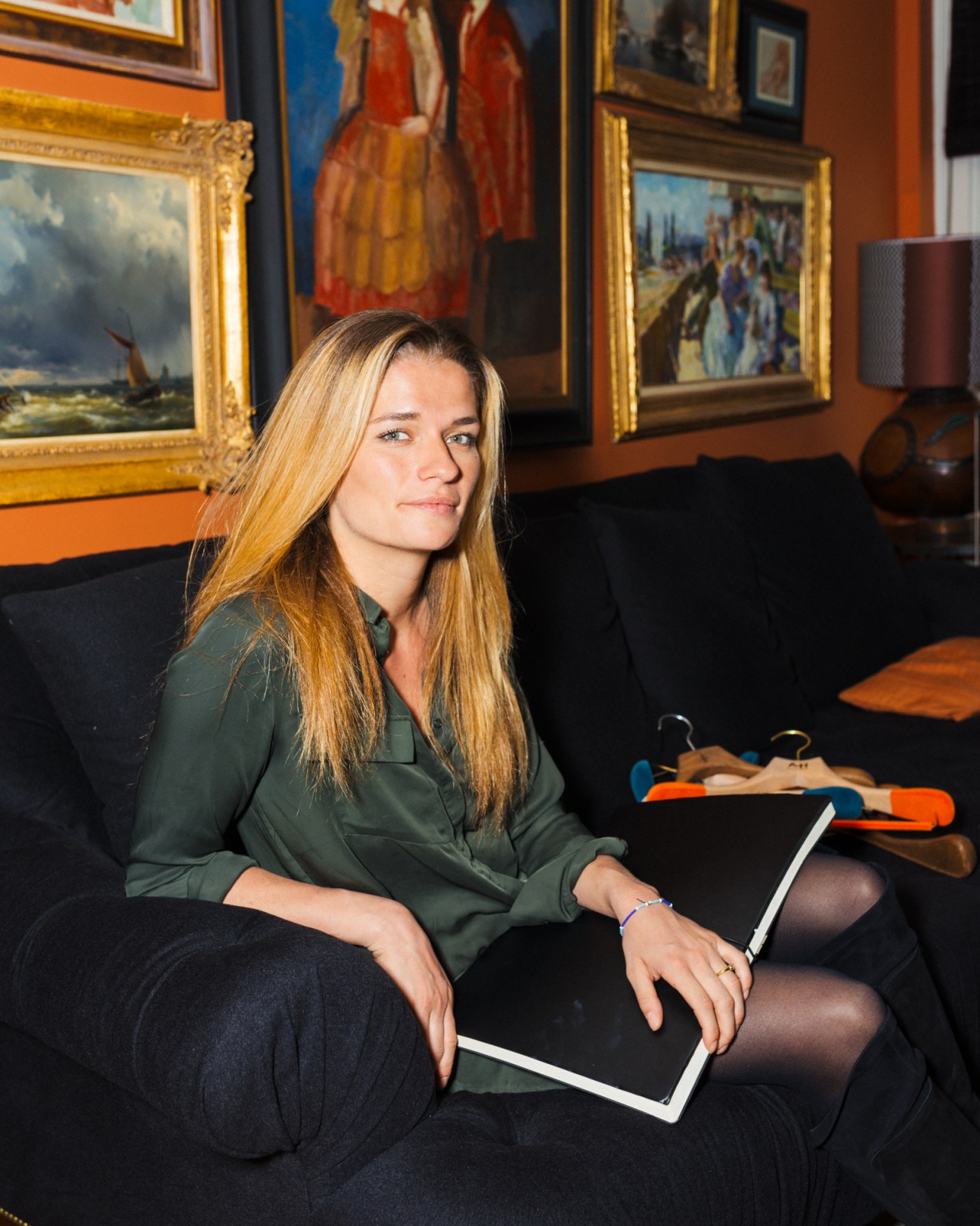 Anne Bas, Arch & Hook co-founder and creative director, sitting with hangers and a tablet in an art-lined room.