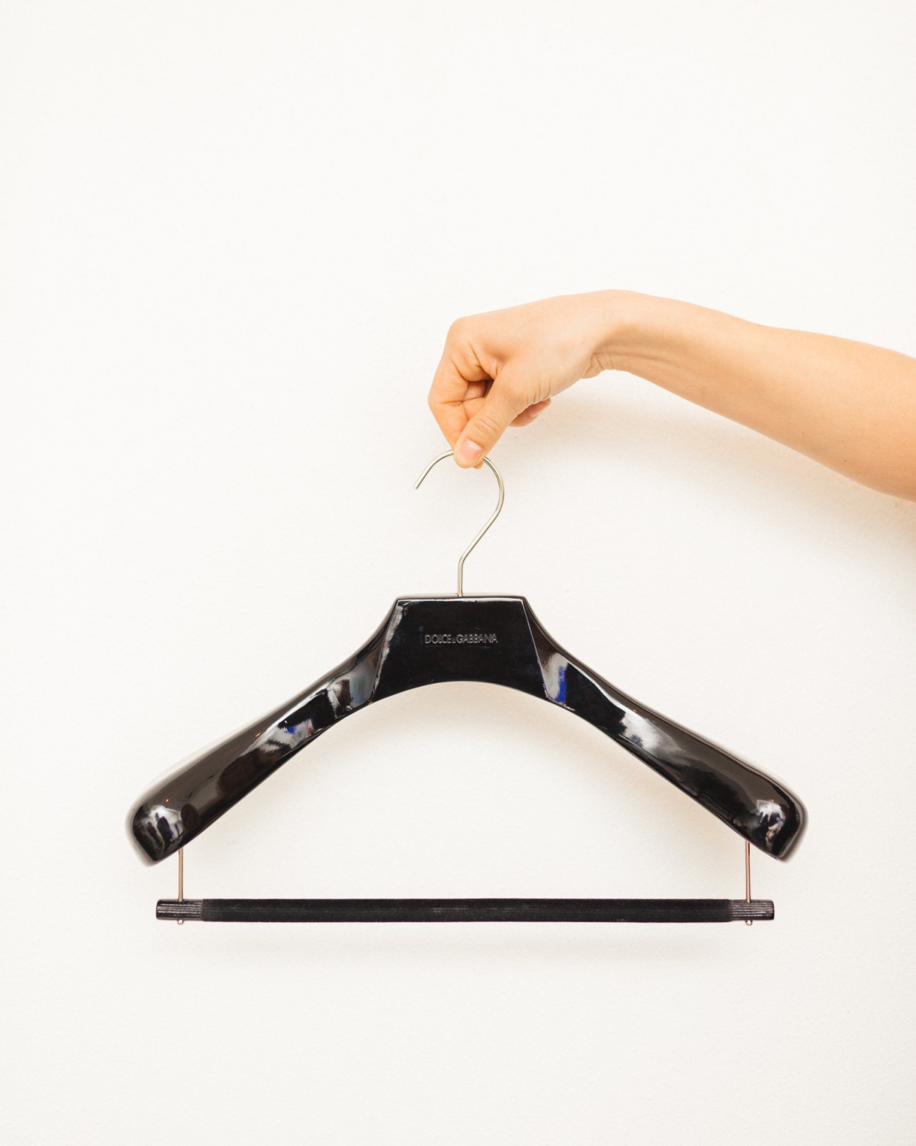 Hand holding a Dolce & Gabbana black wooden hanger against a white background.