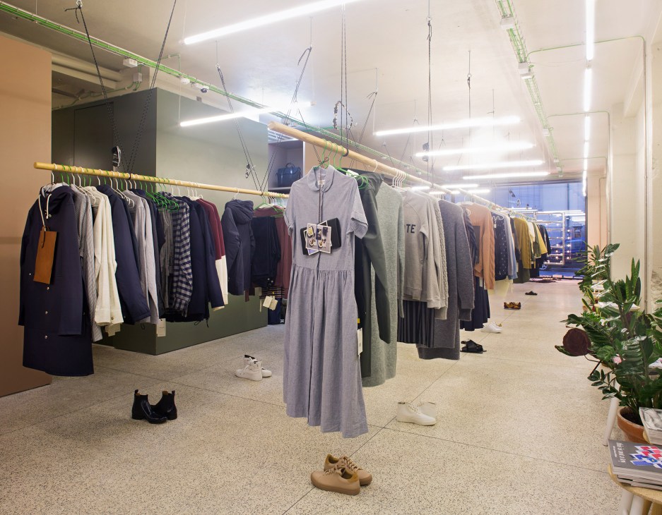 Interior of EarlyMade retail store showing clothes hung on wooden rails suspended from ceiling with ropes.