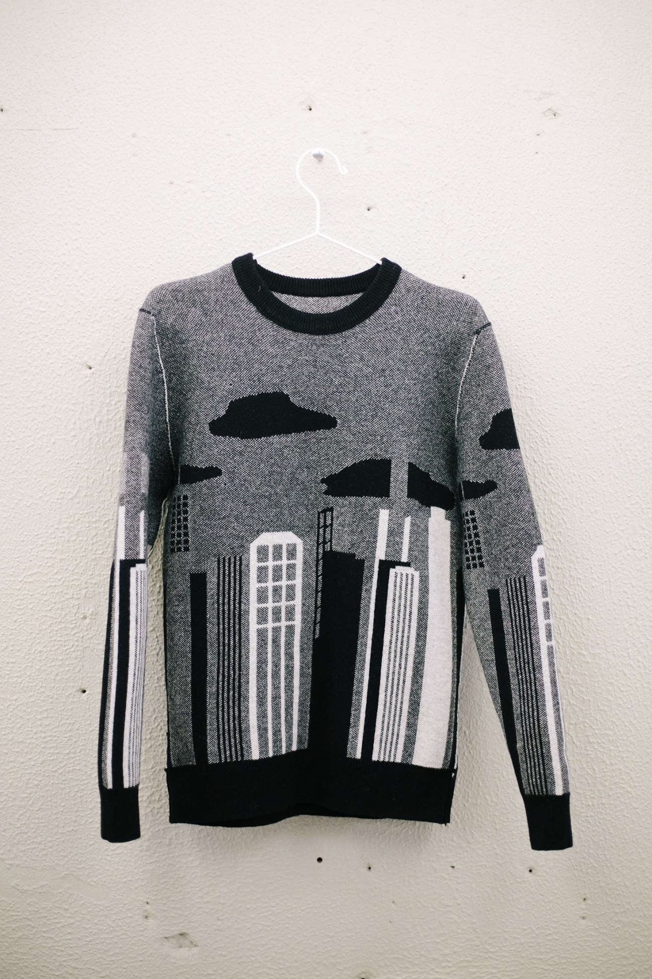 Maison Kitsuné reversible sweater with black and white cityscape knit pattern hung on white hanger.