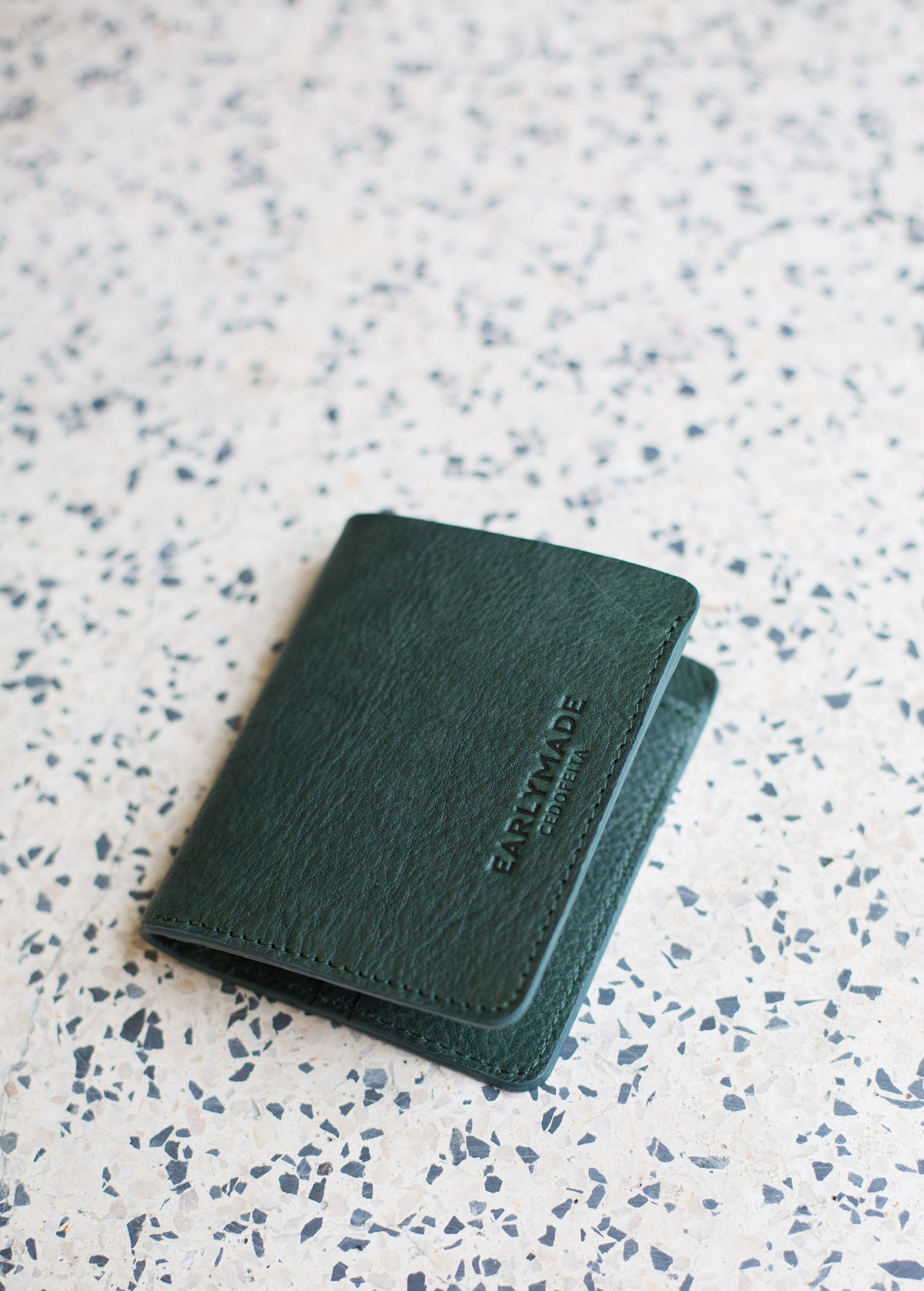 Green leather EarlyMade purse on a speckled white surface.