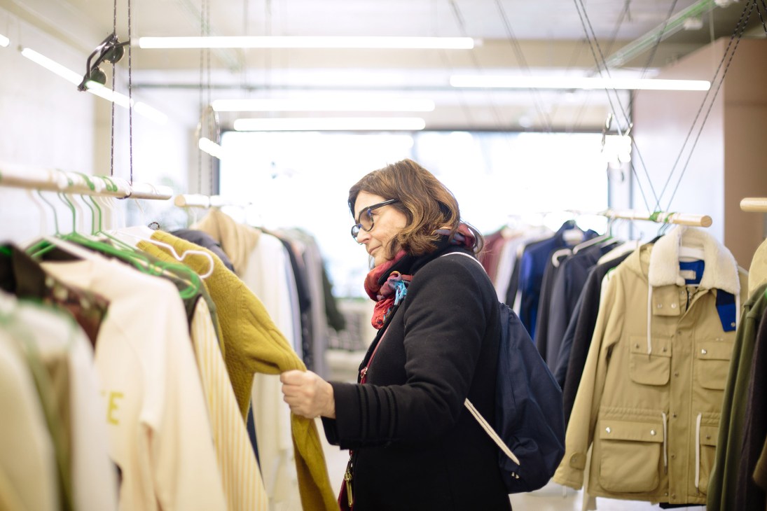 Woman browsing clothing hung on rope rails inside EarlyMade retail shop in Porto.
