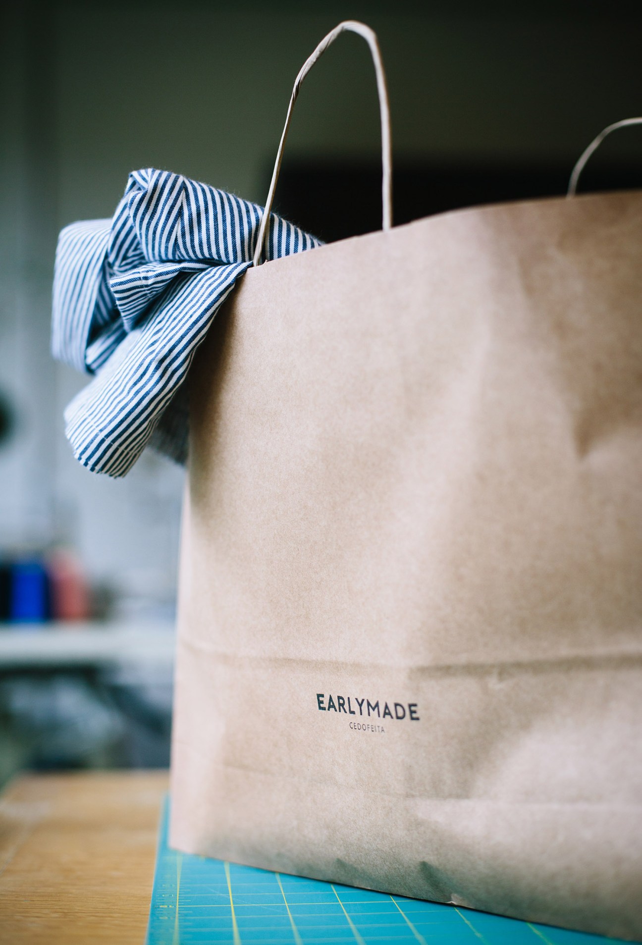 EarlyMade branded canvas tote bag with blue striped ribbon handles on wooden surface.