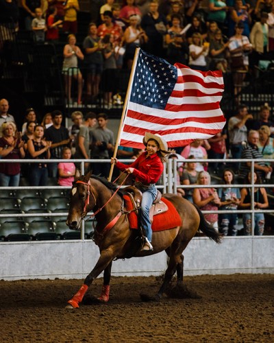 Person on horseback carrying an American flag at Iowa State Fair rodeo arena