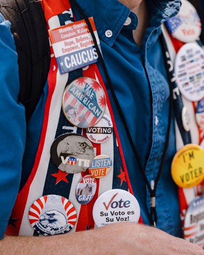Political campaign badges and pins displaying voting messages and candidate names pinned to a person's clothing at Iowa State Fair.