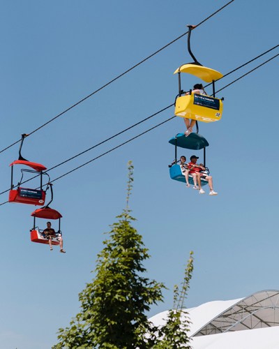 Colorful chair lift cars suspended on cables above Iowa State Fair grounds with trees below.