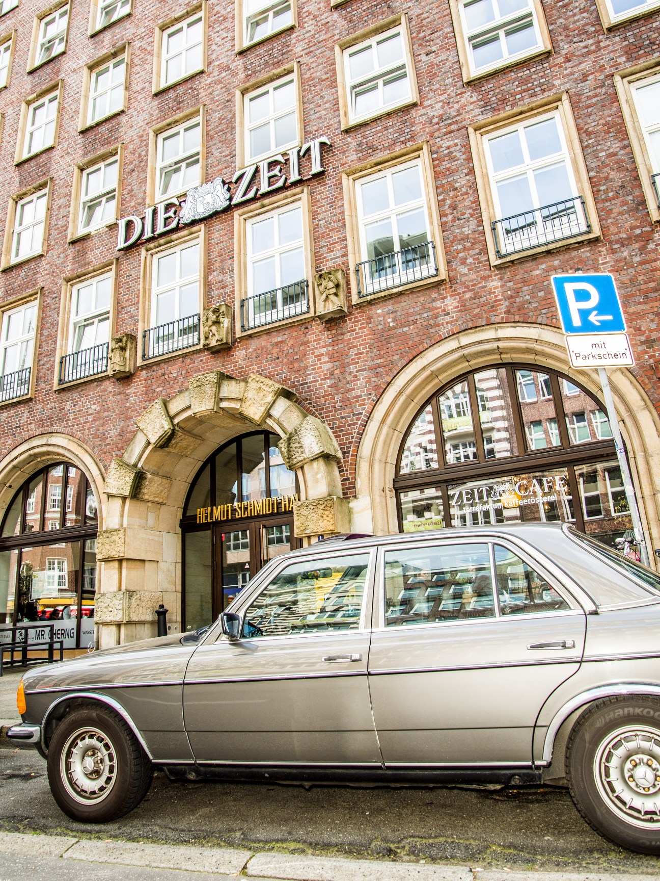 Façade of the Helmut-Schmidt-Haus in Hamburg with Die Zeit signage and a parked sedan.