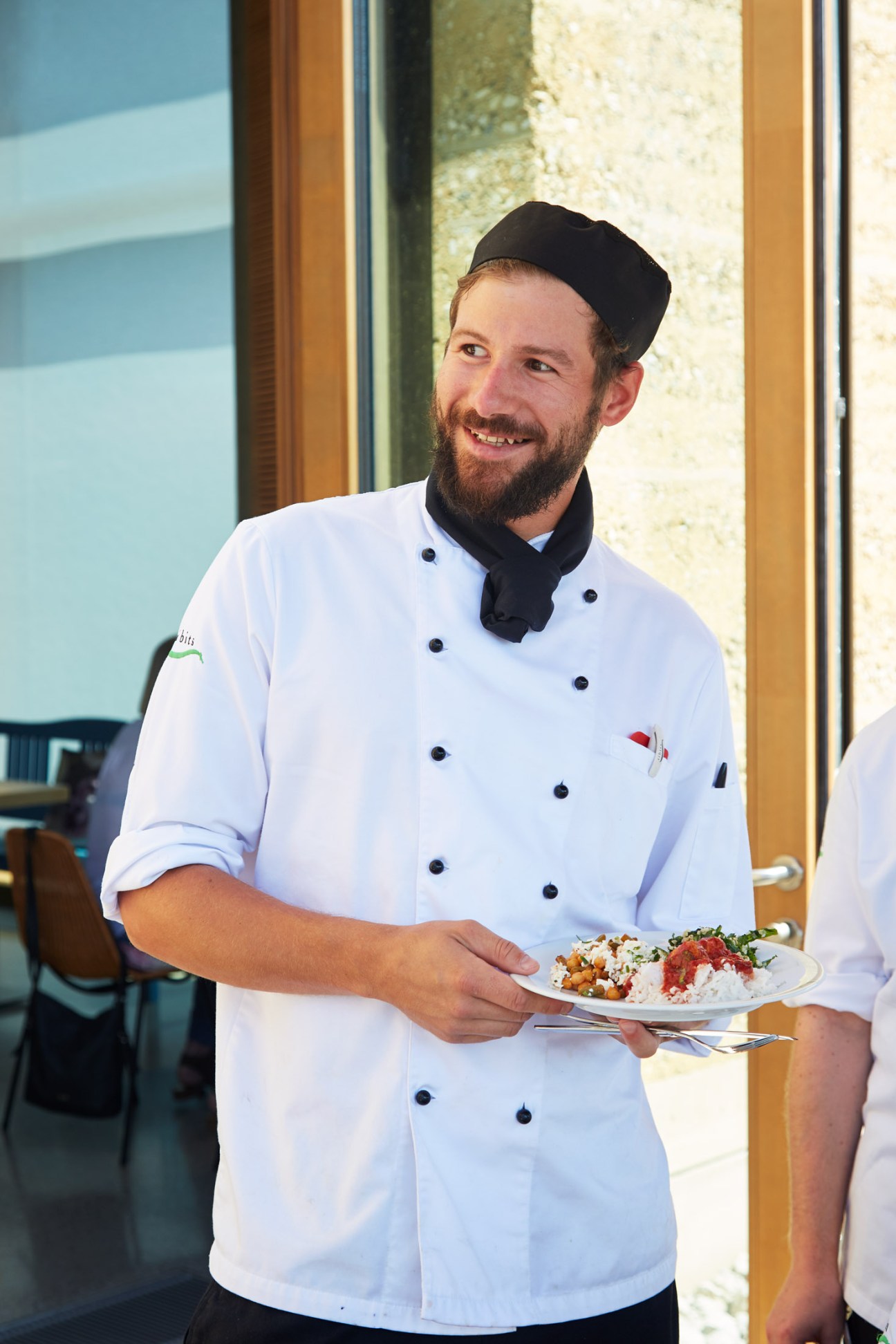 Chef in white uniform holding a plate of vegetarian food at Tibits restaurant