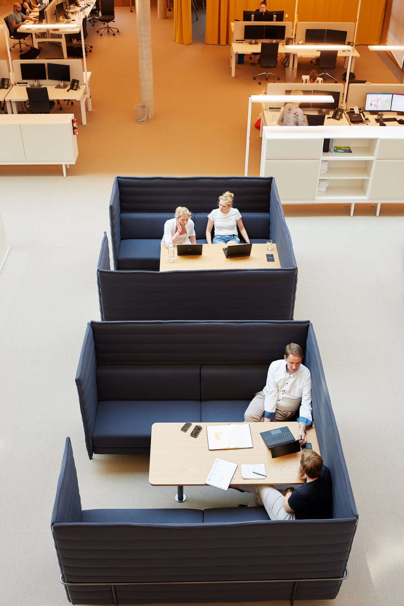 Aerial view of Alnatura Campus office with staff in Vitra high-back sofas designed by Ronan and Erwan Bouroullec, set in open-plan workspace with natural flooring.