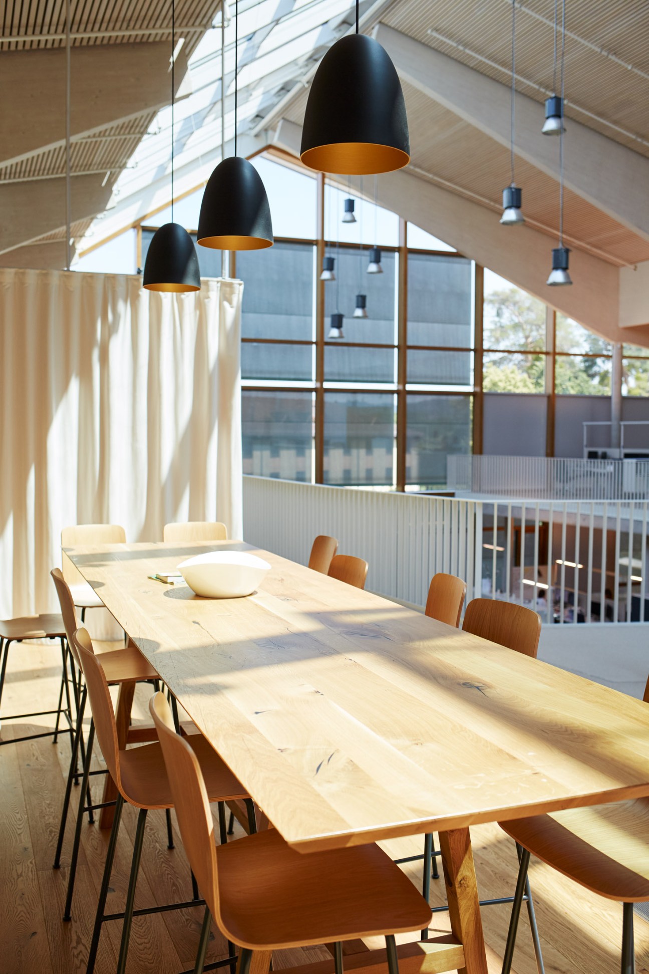 Bright meeting room with wooden table, modern chairs, black pendant lights and floor-to-ceiling windows at Alnatura Campus