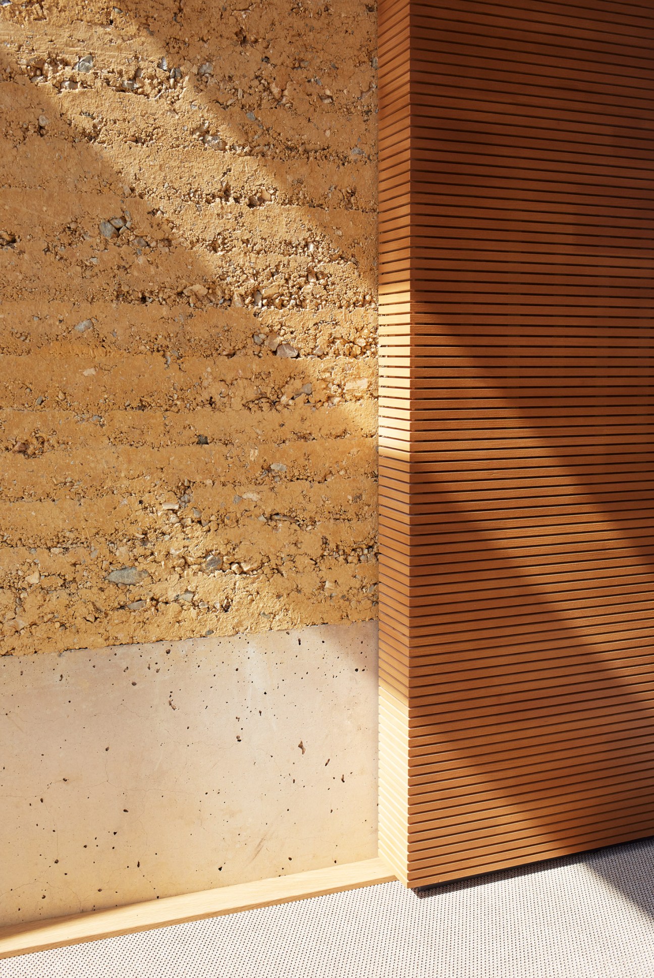 Close-up of rammed-earth wall with natural texture next to wooden cladding panel.