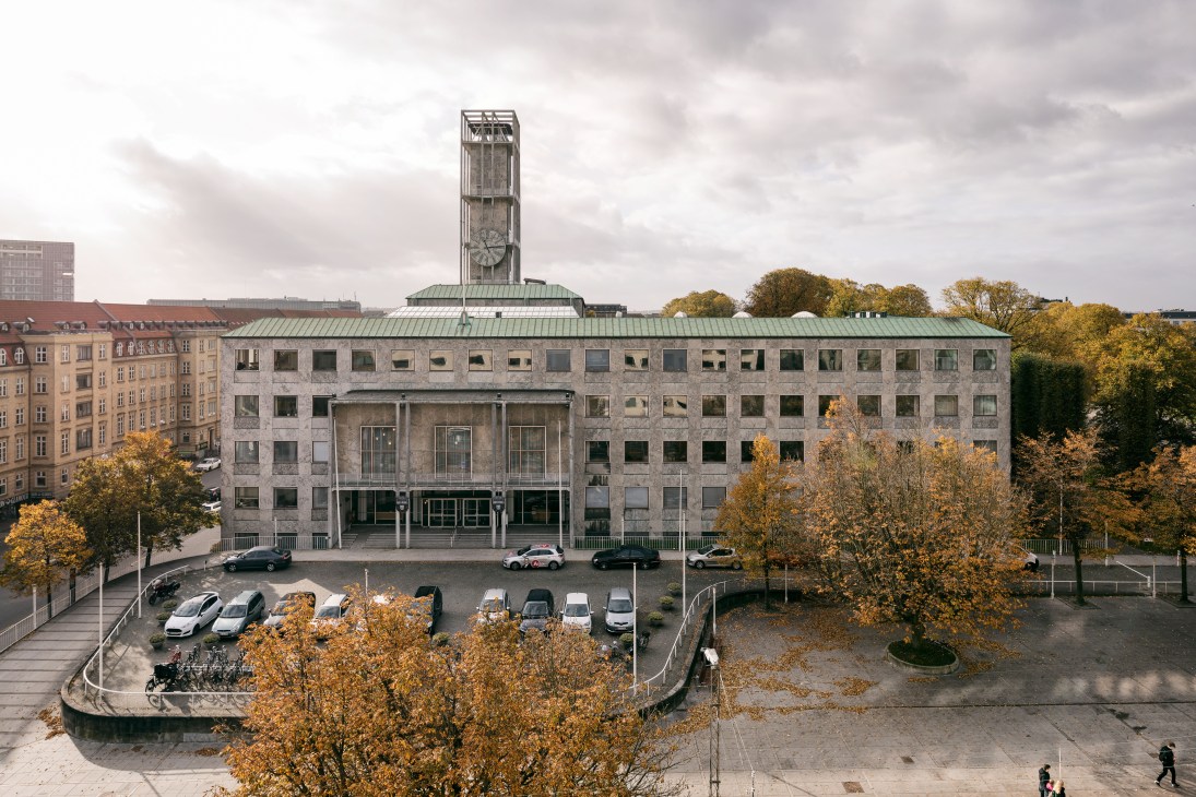 Aarhus City Hall exterior with grey marble facade, clock tower, and autumn foliage surrounding the modernist building.