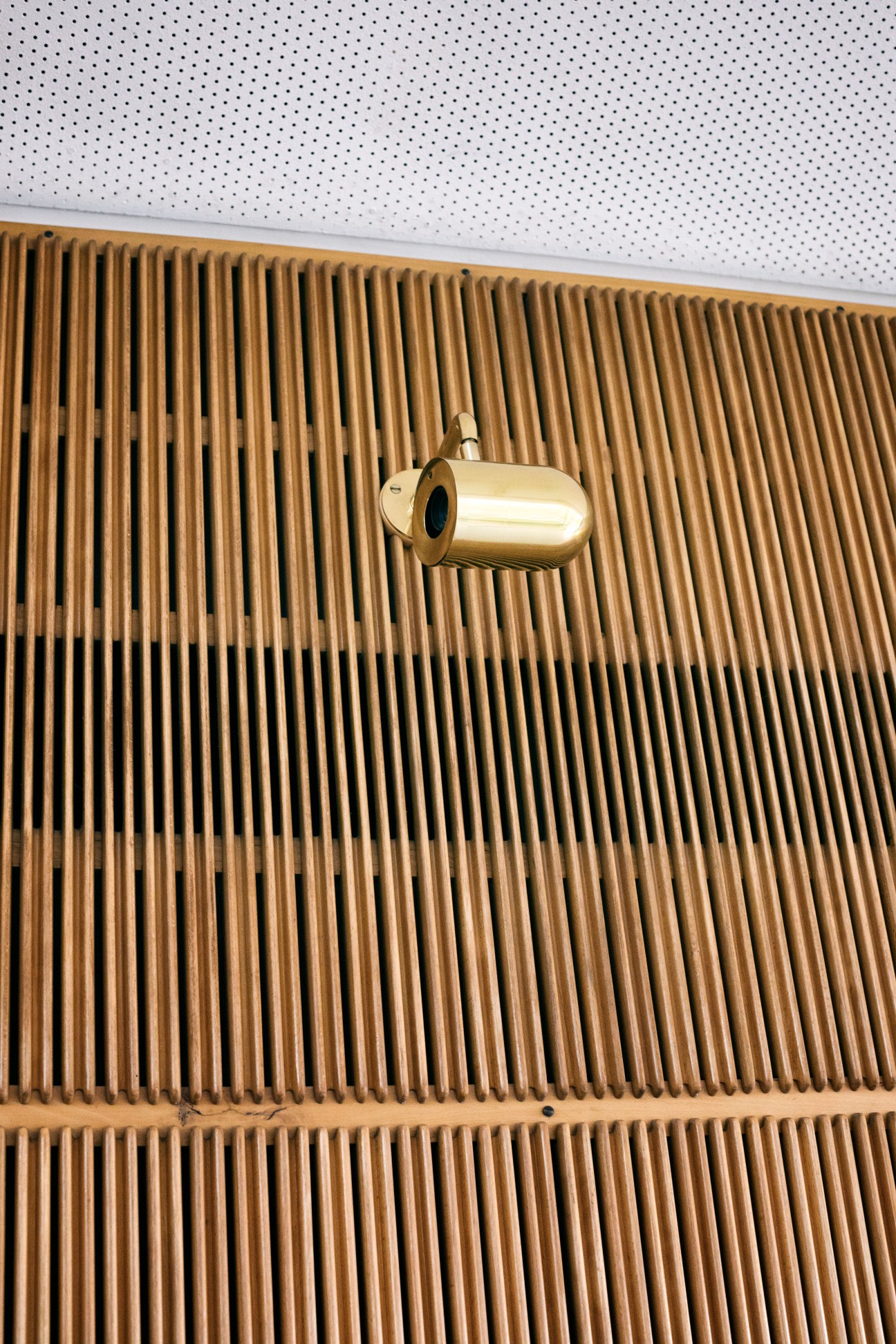 Brass security camera mounted on wooden slat wall panel in Aarhus city hall.