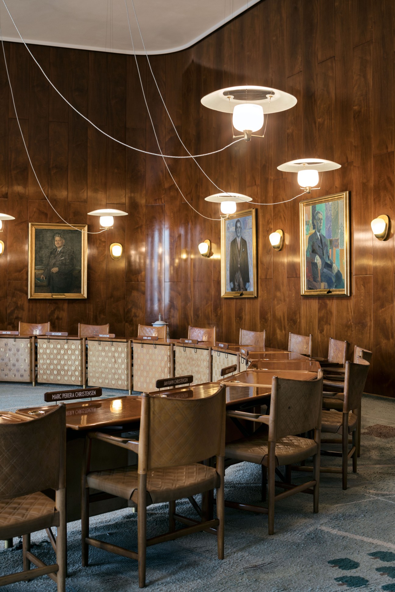 Aarhus city hall council chamber with wood-panelled walls, pendant lights, portraits, and modernist wooden chairs.