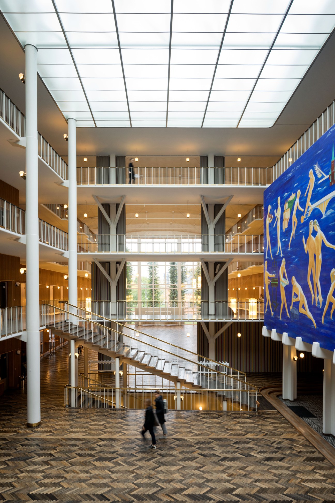 Multi-story atrium of Aarhus City Hall with illuminated ceiling, white columns, metal railings, and blue tapestry.