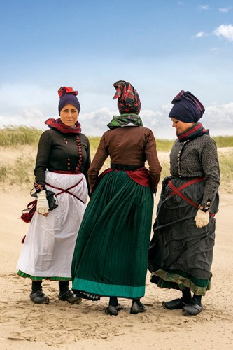 Three women in traditional Danish dress standing on sandy beach