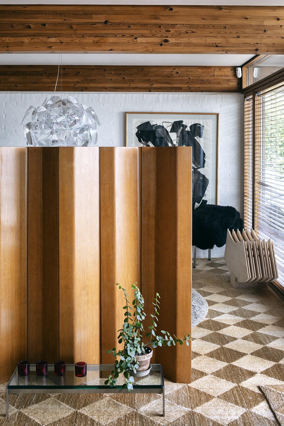 Untreated wooden interior wall panels with aged patina in a modernist home, featuring a small glass table and potted plant.