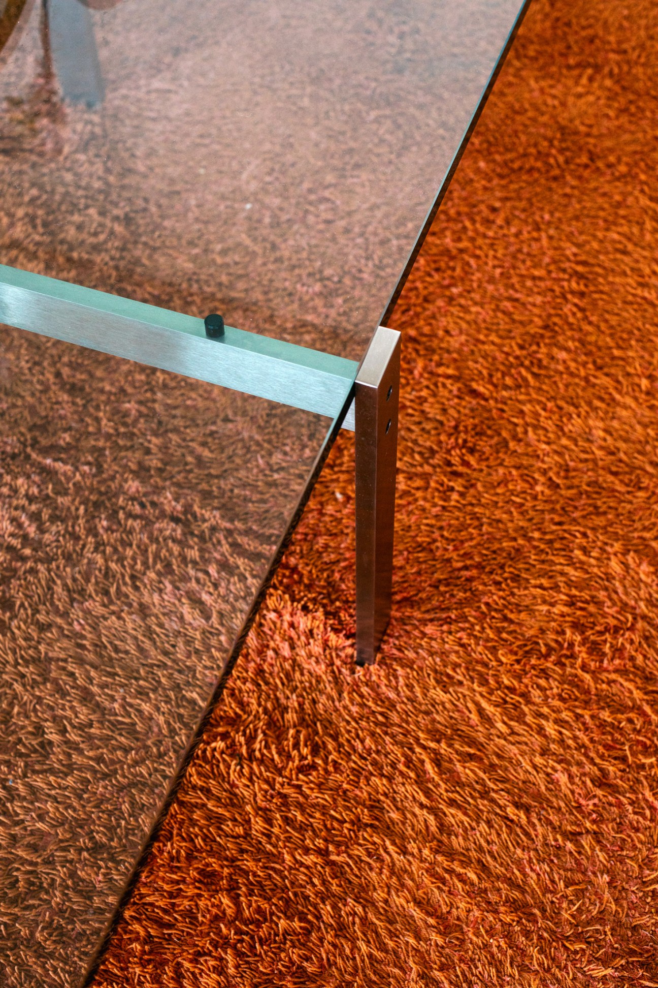 Close-up of Poul Kjaerholm's PK61A side table showing minimalist steel frame and glass top on seagrass flooring.