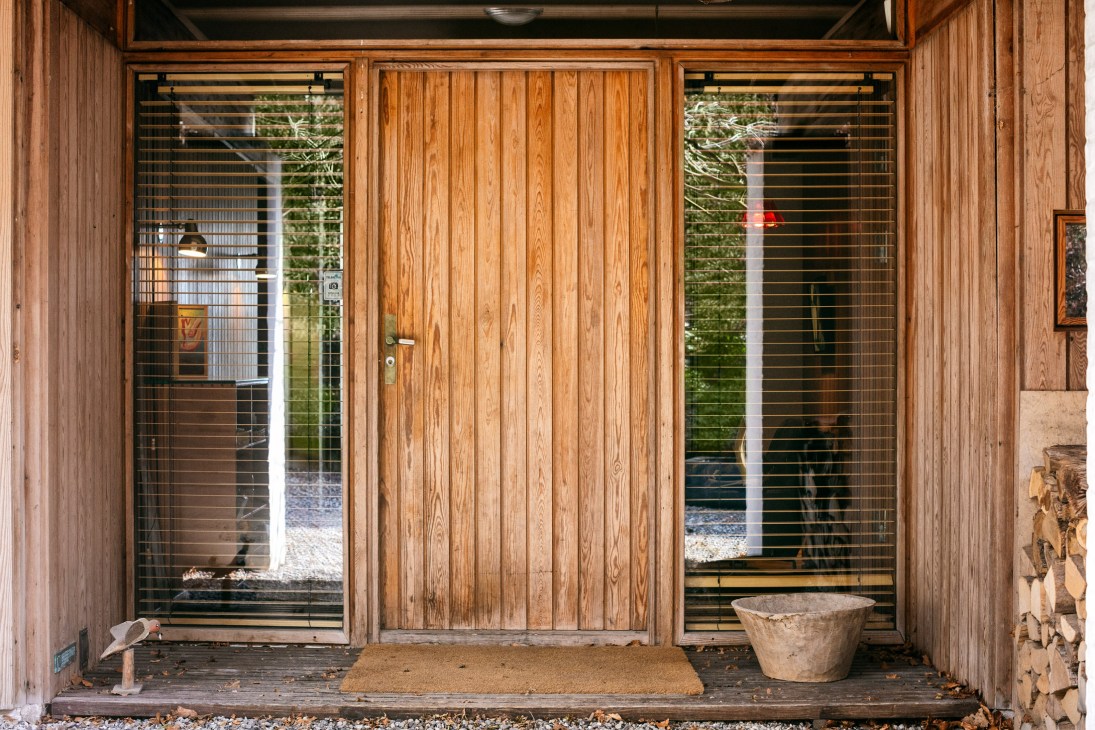 Japanese-inspired house entrance with natural wooden door and glazed panels flanked by untreated timber walls.